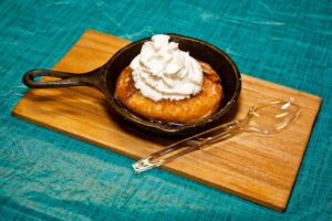 A Photo of a homemade honey bun with whipped cream on top.