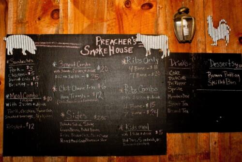 A photo of Preacher's Smokehouse's BBQ Menu which is done in white and colored pastel chalk on a black chalk board.